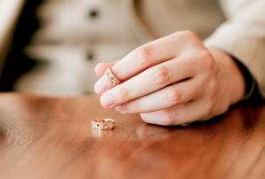 Dłoń oparta na drewnianym stole z obrączkami – symbol sprawy rozwodowej.